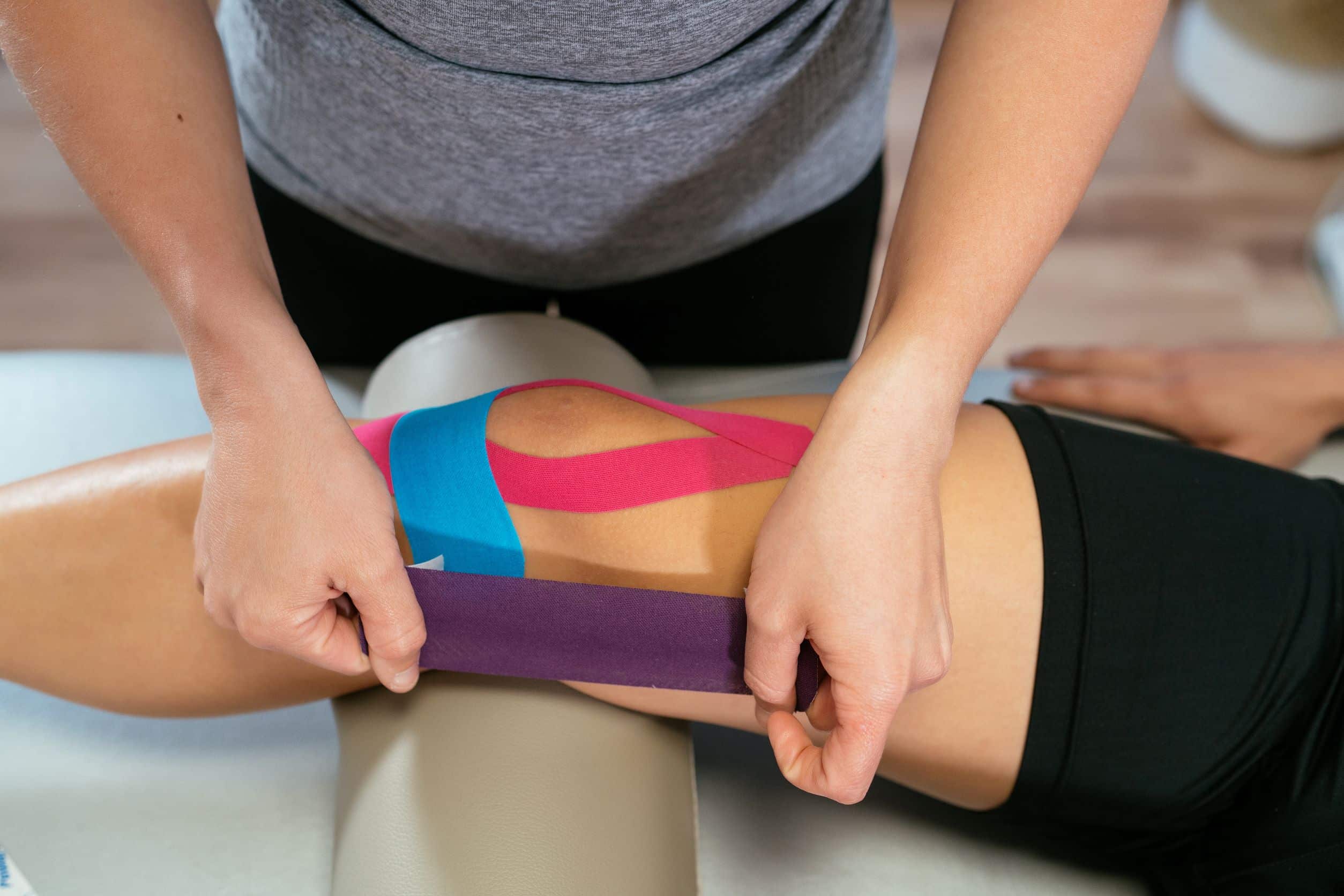 Physiotherapist applying the kinesio-taping technique on a patient's knee.